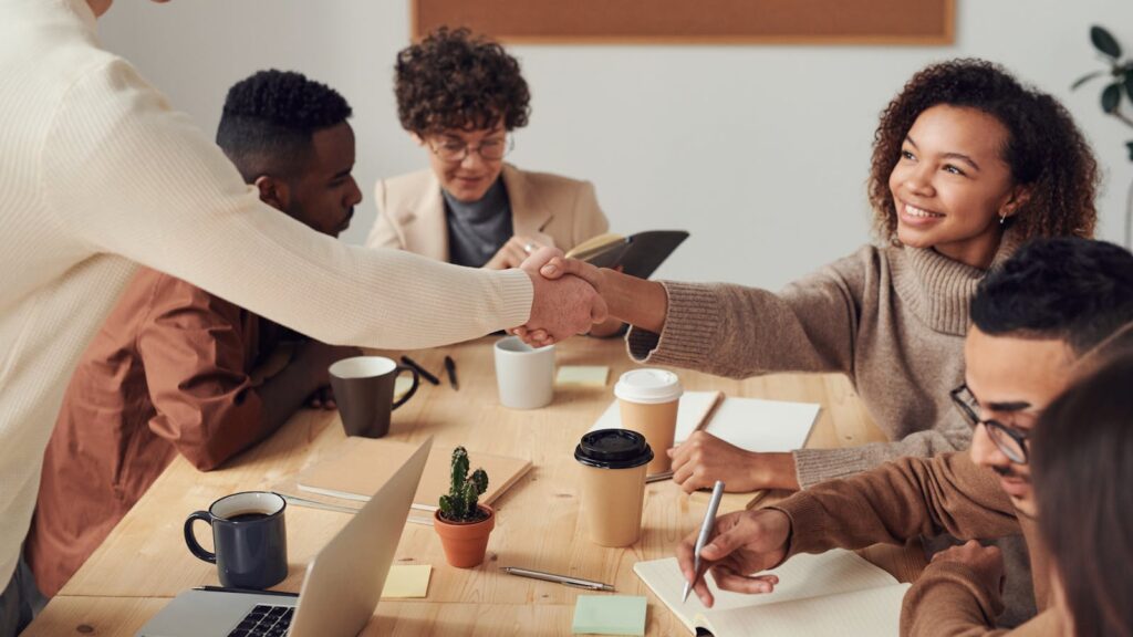 Colleagues collaborating indoors, sharing smiles, and shaking hands during a business meeting.