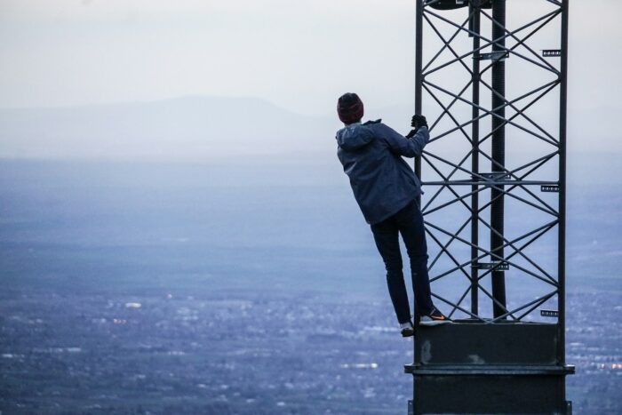 man climbing on tower near buildings at daytime