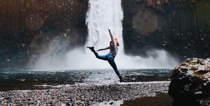 woman jumping in front of waterfalls during daytime